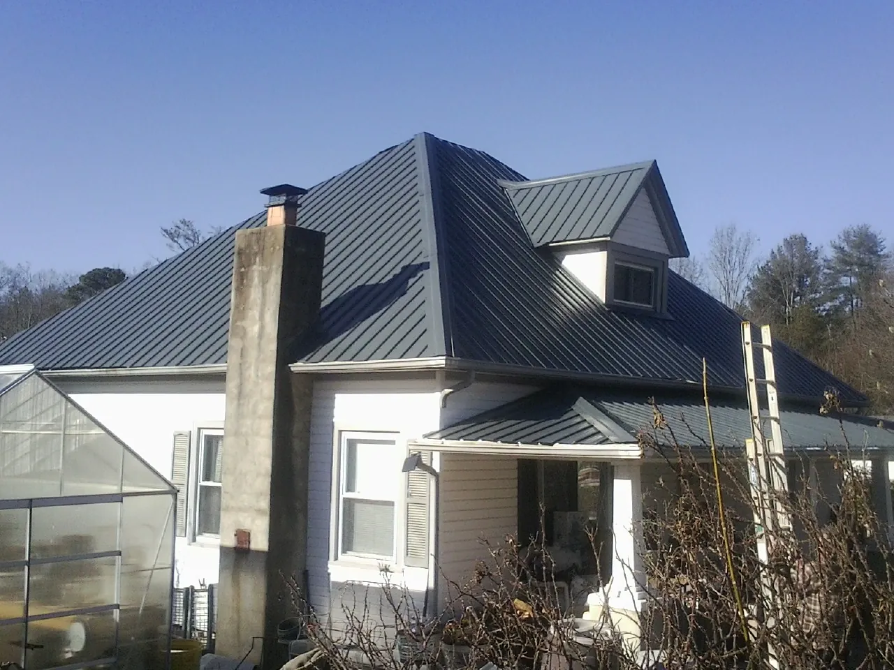 Dark blue standing seam metal roof on a white farmhouse with dormer — Slate & Tile Roof Repair by Roofing Brothers in Shiner