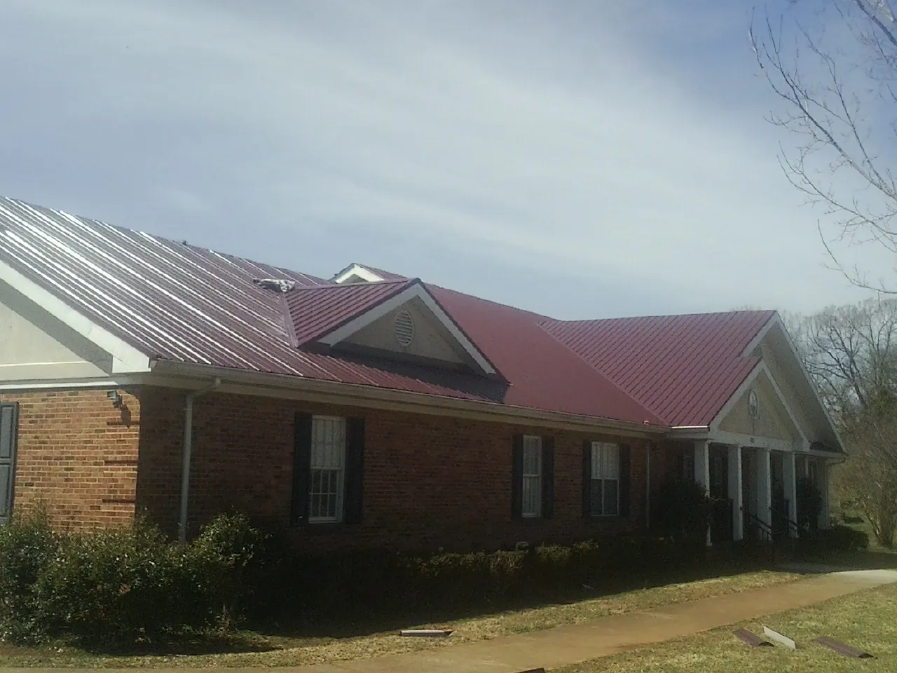 Red metal roof with gabled entries on a long brick building, from a Hail Damage Roof Repair job in Shiner