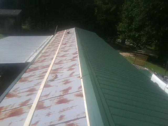 Old rusted panels beside newly installed green metal roofing — Wind Damage Roof Repair by Roofing Brothers in Shiner