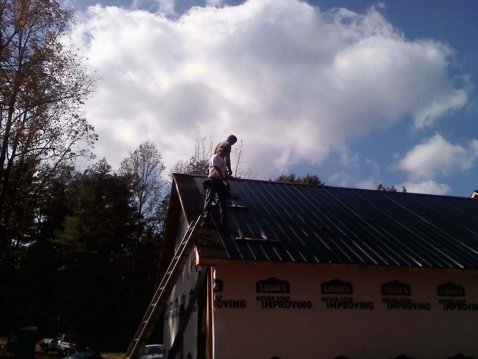 Roofer fastening dark metal panels high against a cloudy sky, from a Roof Inspection job in Shiner