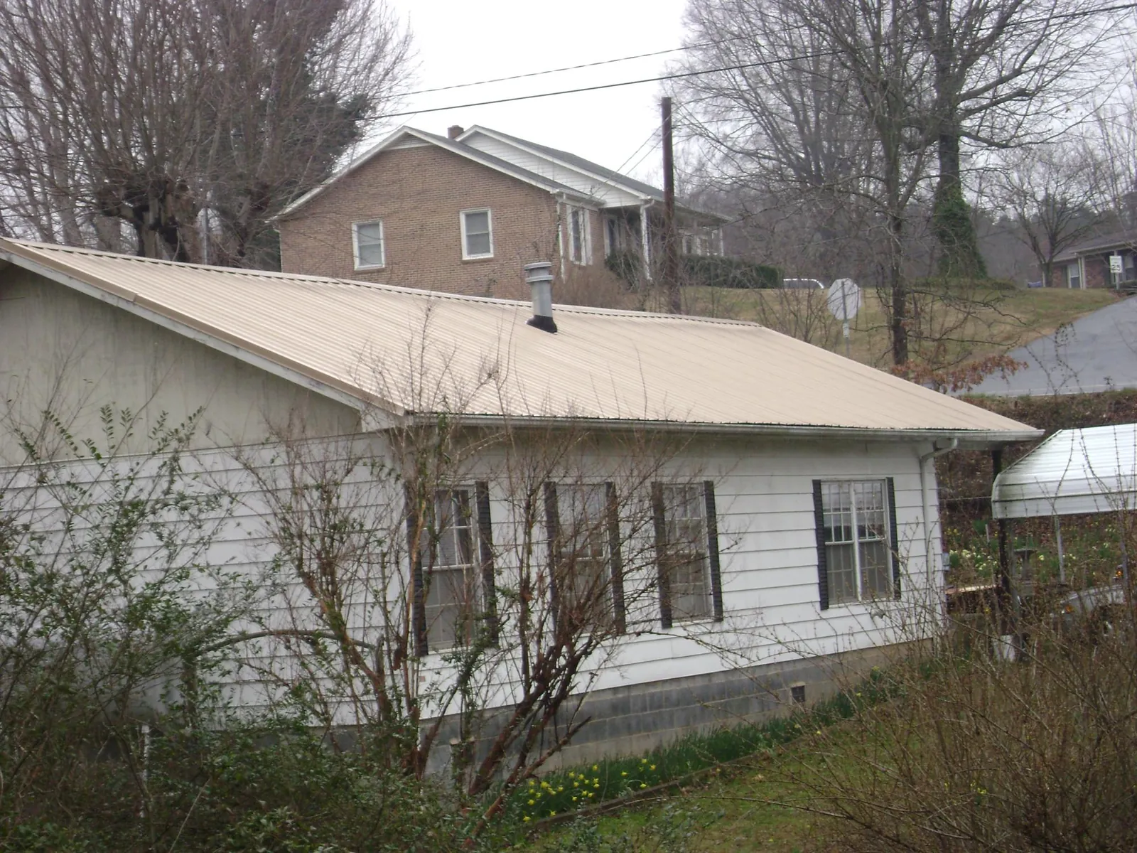 Tan metal roof on a white sided house set into a hillside — Commercial Roofing by Roofing Brothers in Shiner